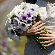 A person holding a bouquet of snow kiss mix anemone flowers in a garden setting.