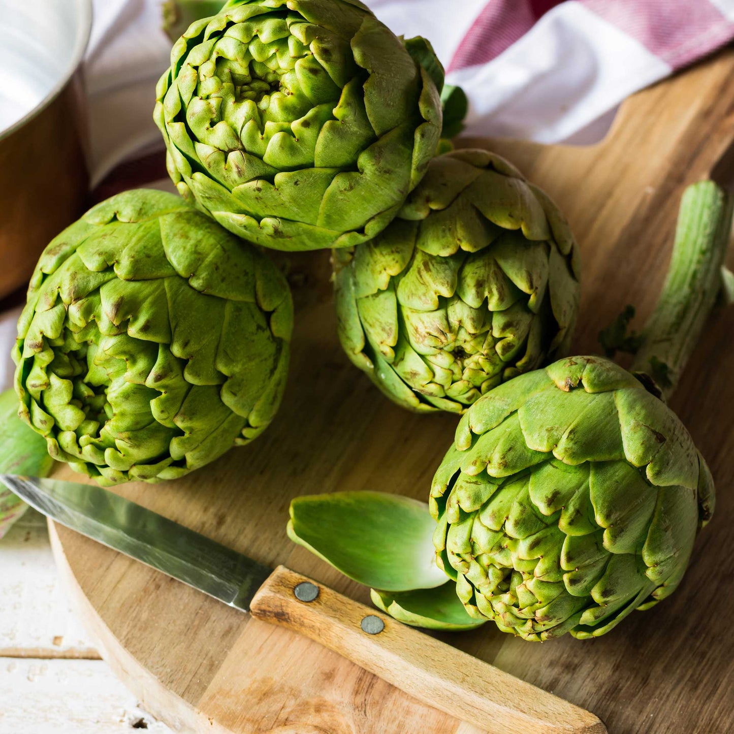 Artichoke tavor heads displayed on a cutting board showing their overlapping green scales.