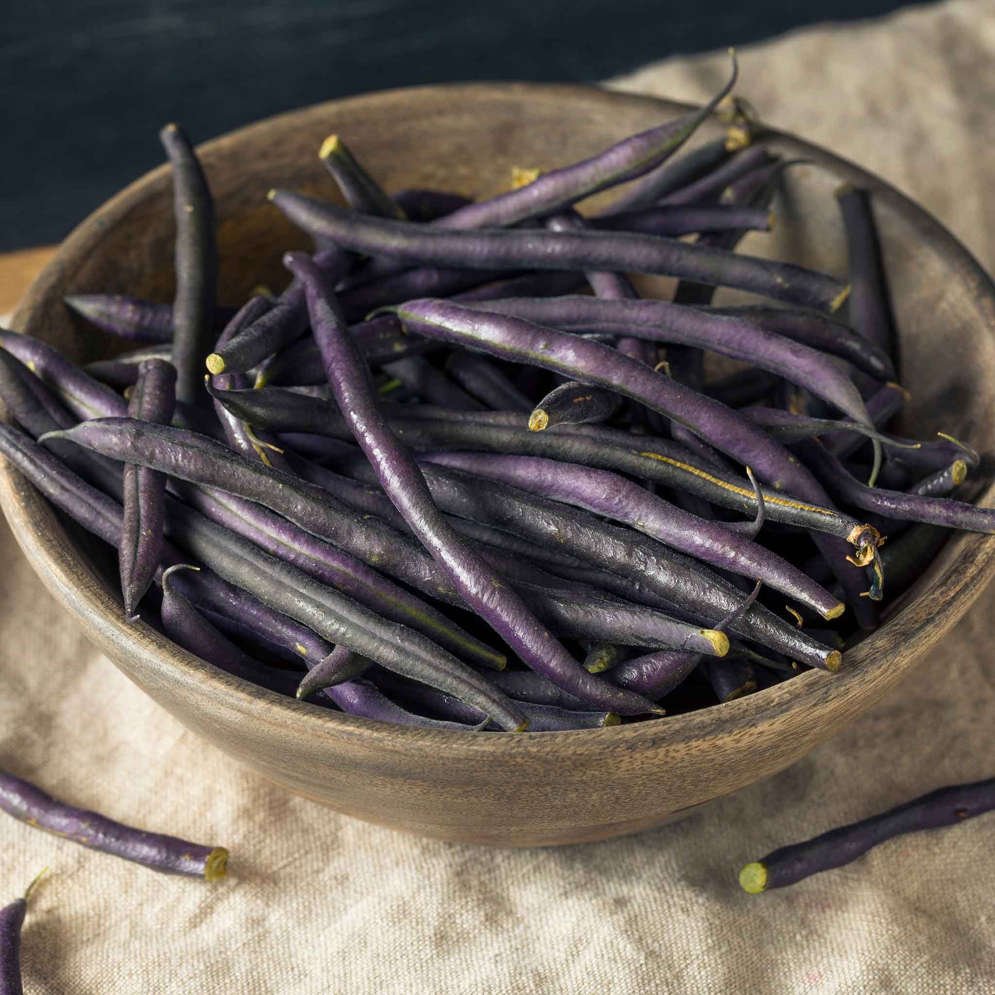 A wooden bowl of purple royal burgundy beans with a neutral background.