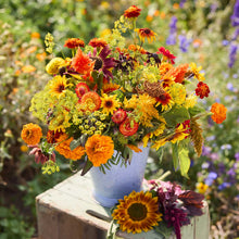 Bouquet of colorful flowers from the summers peak bouquet in a white vase on a wooden stool with a garden background.