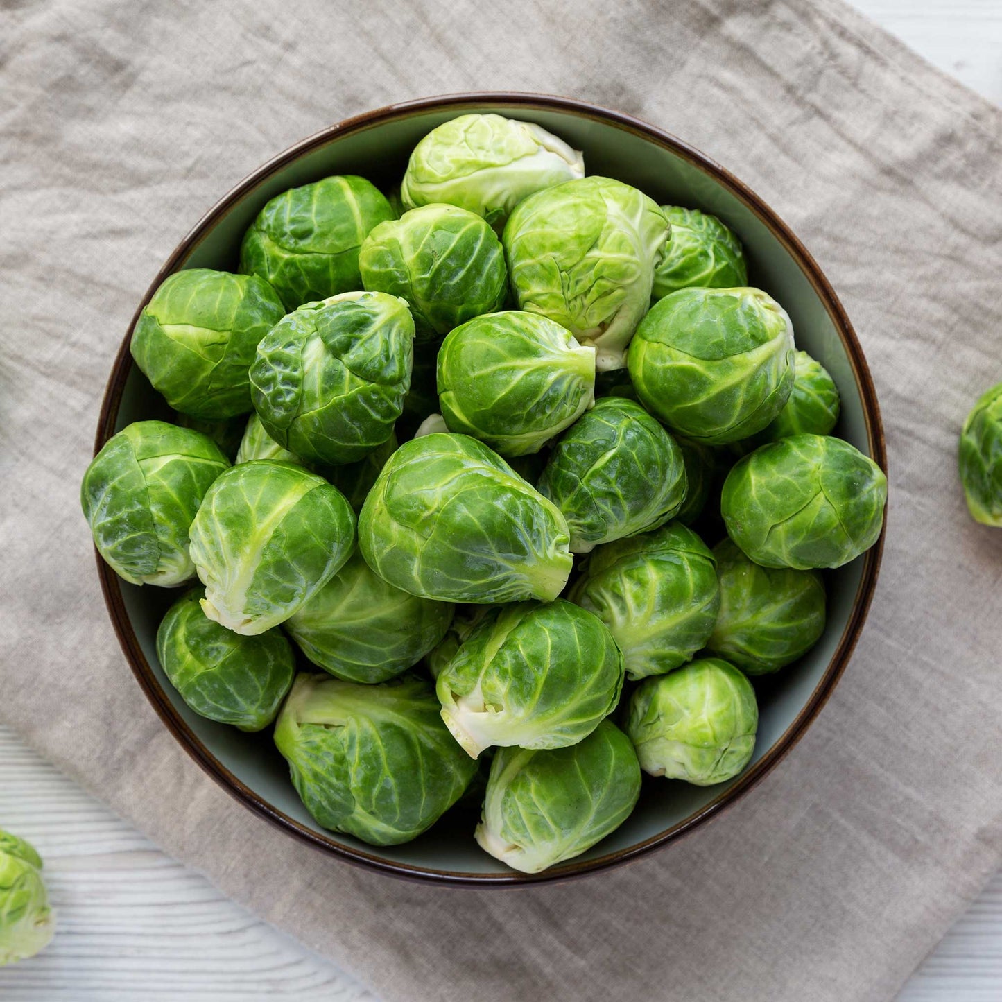 A bowl of several green Dagan F1 brussels sprouts showing layered leaves on a neutral cloth