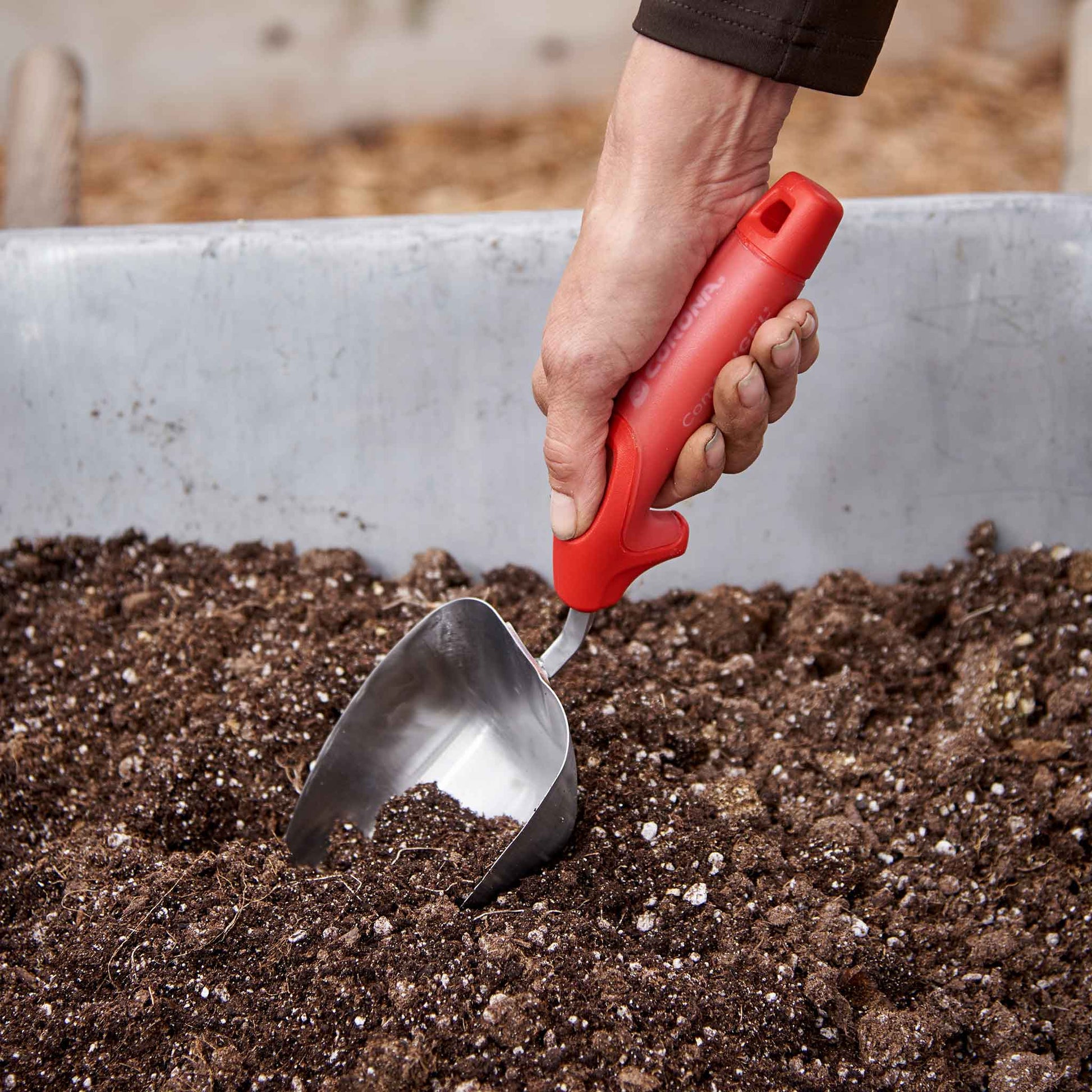 Person gardening with a red handled corona comfortgel scoop in a garden bed with soil.