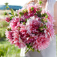 A person holding a bouquet of Otto's Thrill dahlia flowers in a garden setting.
