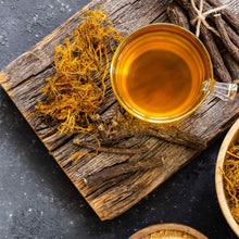 Sprigs of dried licorice root next to licorice tea and dried yellow flowers.