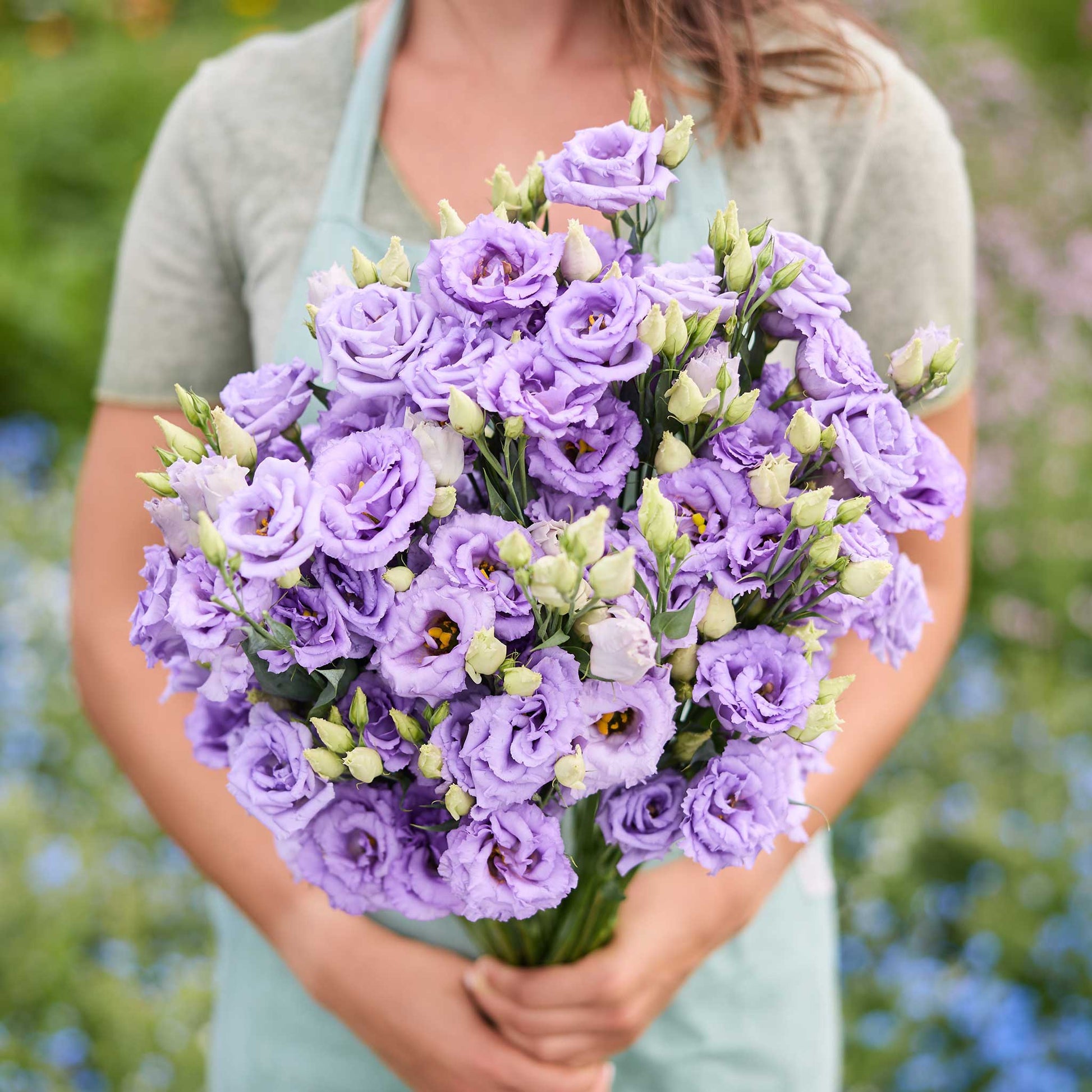 A person holding a bouquet of lisianthus corelli lavender flowers in a garden setting.