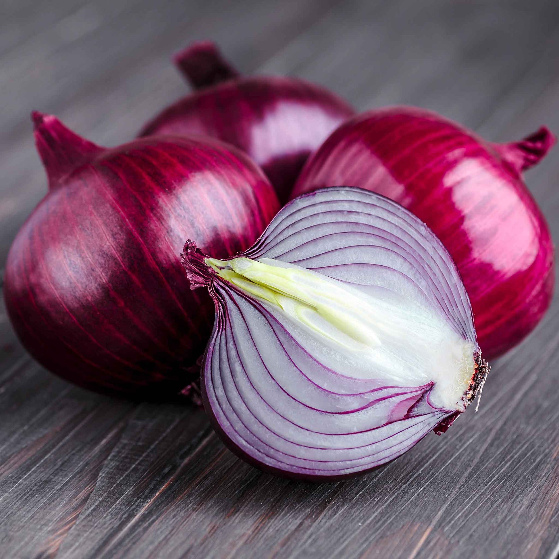 Several vibrant ruby red onions with a papery skin and vibrant interior, resting on a white background.