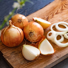 Yellow Stuttgarter onions on a wooden cutting board with some sliced.