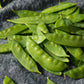 A close-up of Dwarf Grey Sugar pea pods, showing its vibrant green color and the smooth, round peas inside.
