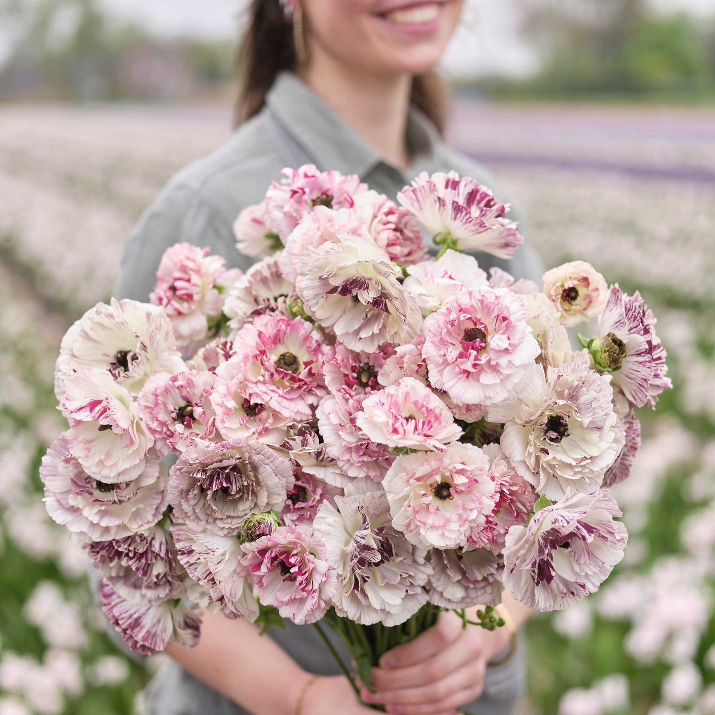 A person holding a bouquet of the ranunculus brushmark cesar and galthie bundle in a natural setting
