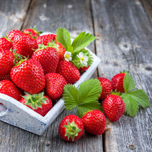 Fresh honeoye strawberries with green leaves on a wooden surface