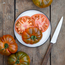 Slices of Black Brandywine tomato with hints of green and brown on its skin, shown on a plate.