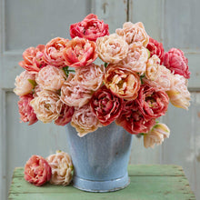 Bouquet of pink and peach flowers from the copper image and pink mist tulip bundle in a rustic blue bucket on a wooden surface.