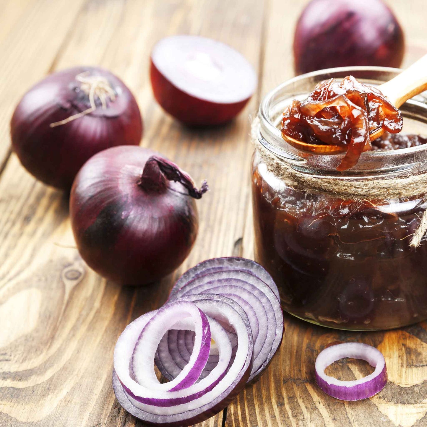 A close-up of several sliced Red Carpet onions with thin, papery skins, resting on a rustic wooden surface.
