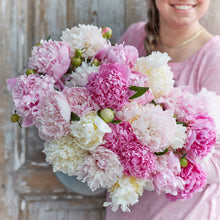 A person holding a bouquet of fluffy pink mix peony flowers with a wooden background.
