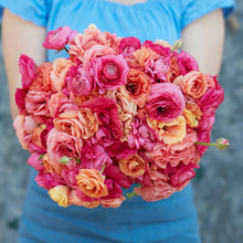 Pink and orange ranunculus lipstick mix bouquet held by a person outdoors